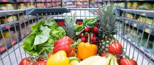 Ein Einkaufskorb mit Obst und Gemüse steht in einem Supermarkt.