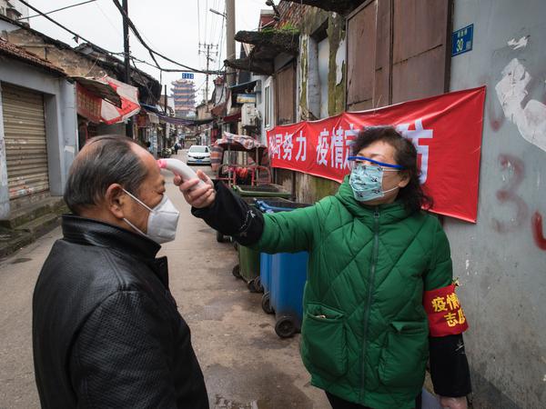 Ein Bild aus Anfangszeiten: Am 7. Februar 2020 misst in Wuhan eine Gemeindemitarbeiterin mit einem Fieberthermometer die Körpertemperatur eines Passanten.|