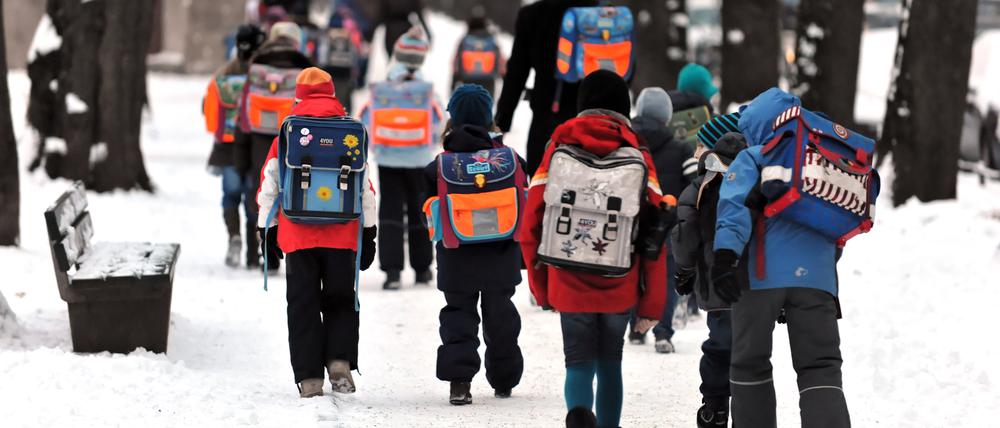 Kinder gehen mit ihren Schulranzen über verschneite Gehwege zu einer Schule in München.