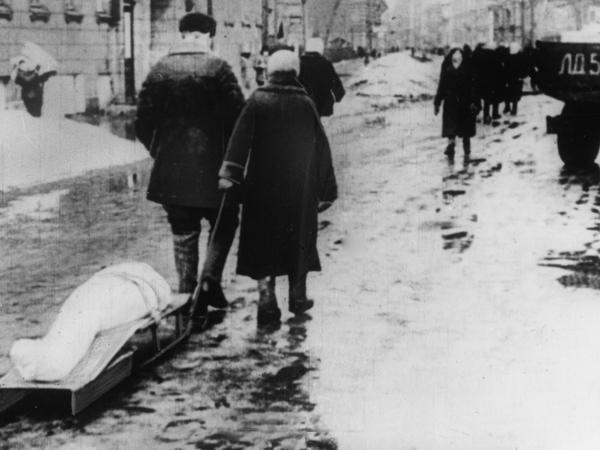 Menschen ziehen einen Leichnam auf einem Schlitten durch eine winterliche Straße.
