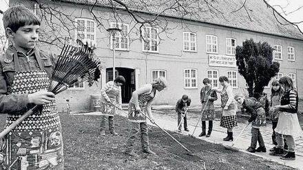 Mädchen und Jungen eines Stralsunder Kinderheims harken in den 1980er Jahren auf dem Heimgelände.