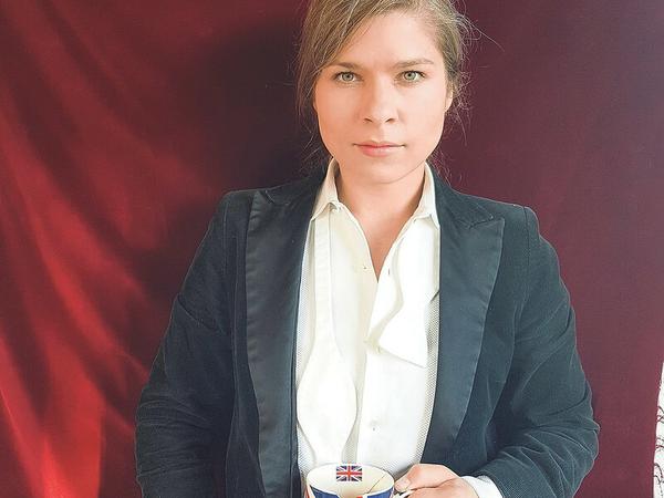 Ein Selbstporträt der Autorin Nele Pollatschek, auf dem sie einen beschädigten Kaffeebecher mit der britischen Flagge in der Hand hält.