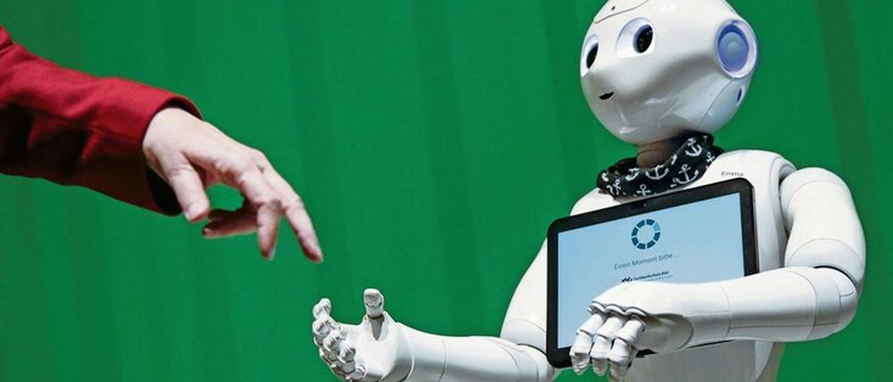 Vor einem grünen Hintergrund treffen sich eine menschliche Hand und die Hand eines Roboters.