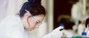 Eine junge Wissenschaftlerin pipettiert im Labor und hält dabei einen Tablett-Computer in der Hand.