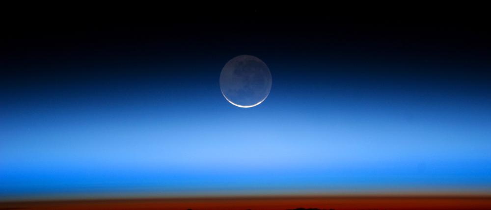 Der Mond, aufgenommen von der Internationalen Raumstation. Die helle Sichel wird von der Sonne beschienen, der blasser erscheinende Teil von der Erde.