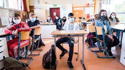 Siebtklässler sitzen in einem Klassenraum an ihren Tischen und tragen Mund-Nasen-Schhutz.