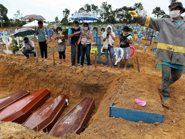 Maskierte Menschen stehen um ein Massengrab in einem Friedhof in Manaus.